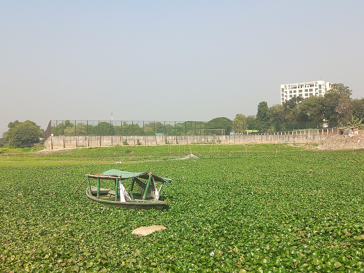 Dhaleshwari River has almost dried up. A boat is stranded mid-river. Right behind it, the Sheikh Russel Mini Stadium is visible, built on land encroached from the river. Recently at  Bhagalpur, Savar upazila, Dhaka