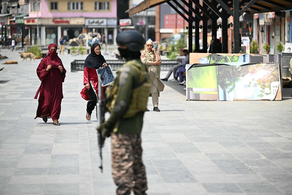 Kashmiri women walk along a road as an Indian paramilitary personnel stands guard in Srinagar on 7 May 2025, following border tensions
