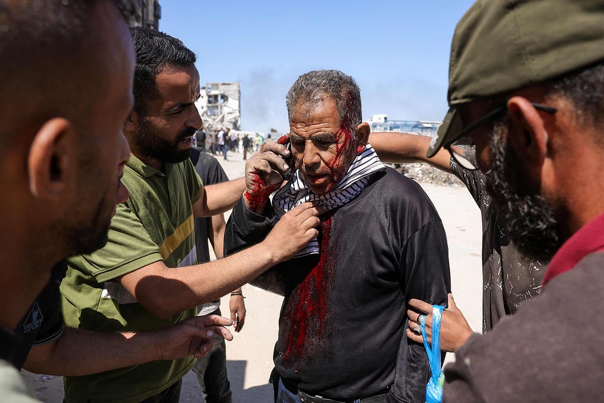 Palestinians tend to an injured man as he speaks on his mobile phone following an Israeli drone strike in Jabalia, in the northern Gaza Strip on 23 May, 2025