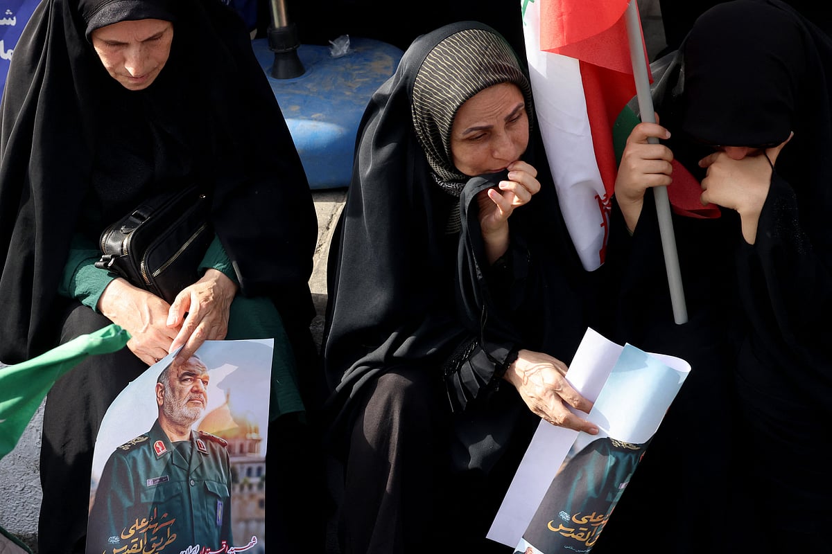 Women mourners holding posters of Iranian Islamic Revolutionary Guard Corps (IRGC) commander Hossein Salami sit on the edge of the pavement watching the funeral of the Iranian Revolutionary Guards commander and other military commanders killed during Israeli strikes on Iran, during their funeral procession at Enghelab (Revolution) Square in the capital Tehran on 28 June, 2025.