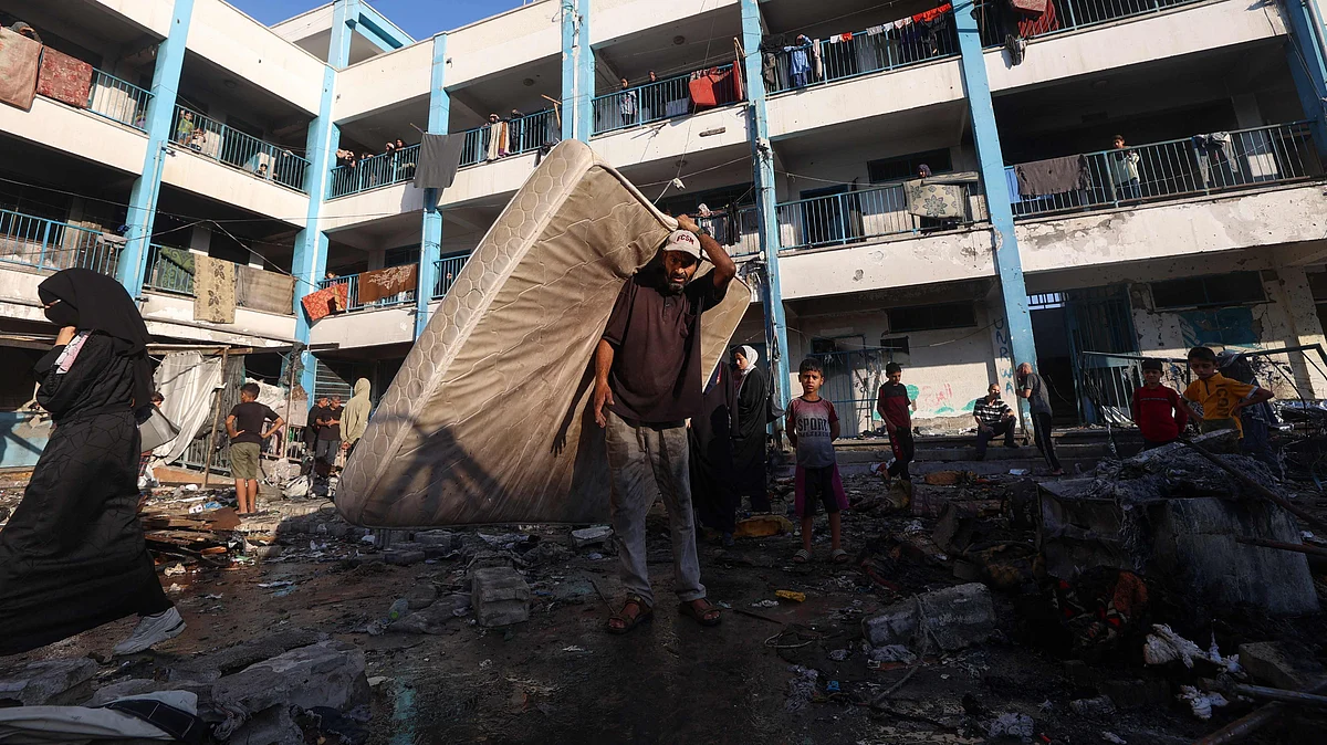 A Palestinian man carries a mattress after an Israeli strike which hit a school sheltering displaced Palestinians in the Al-Bureij camp in the central Gaza Strip on 8 July, 2025