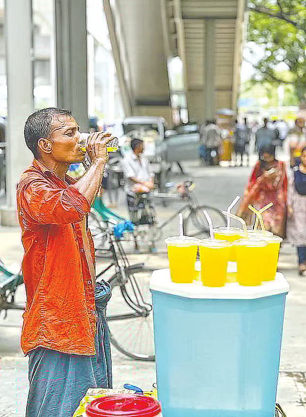 A rickshaw puller drinks juice on the roadside sidewalk to cope with the extreme heat. The photo was taken in the Agargaon area of Dhaka.