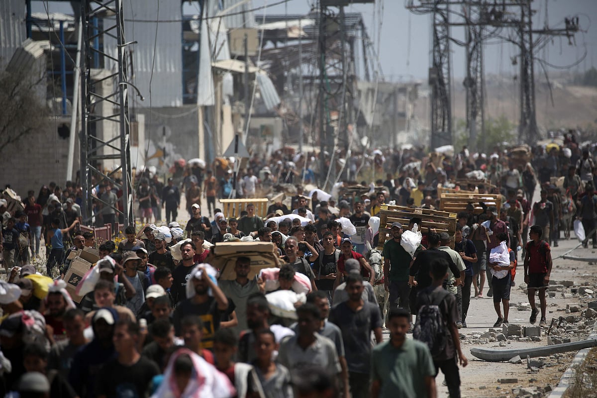 Palestinians return to the Nuseirat refugee camp from a US-backed Gaza Humanitarian Foundation distribution point near the Netsarim corridor in the central Gaza Strip, some carrying food parcels and others wooden pallets for burning, on 27 July 2025.