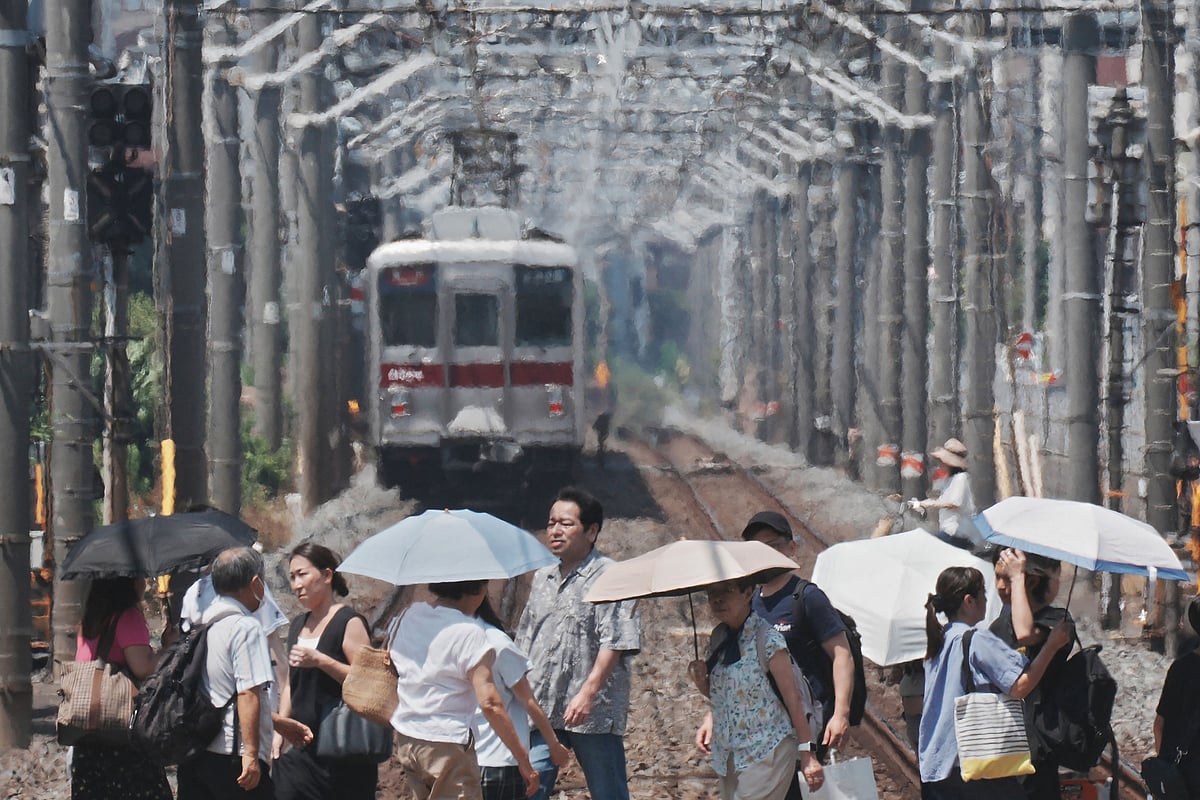Heat haze is seen in the background while pedestrians with umbrellas cross a railroad on a hot day in Tokyo on 5 August 2025.