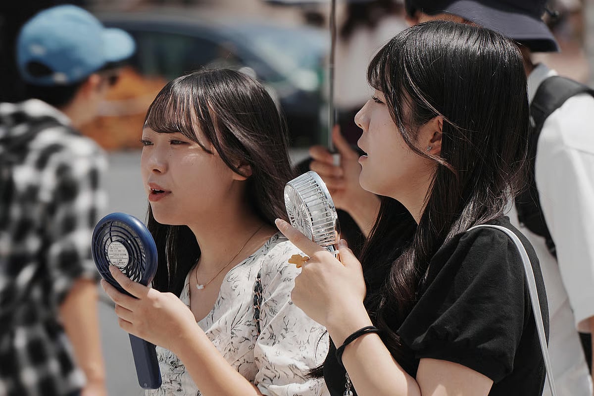 Pedestrians use their handheld fans on a hot day in Tokyo on 5 August, 2025.