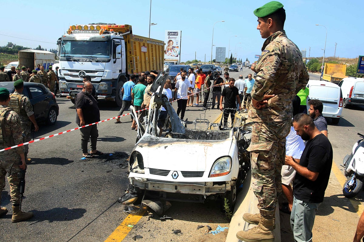 Lebanese army soldiers and onlookers stand near the wreckage of a vehicle that was reportedly targeted by an Israeli strike, on the highway near the village of Ansarieyh, south of the coastal city of Sidon on 8 August 2025.