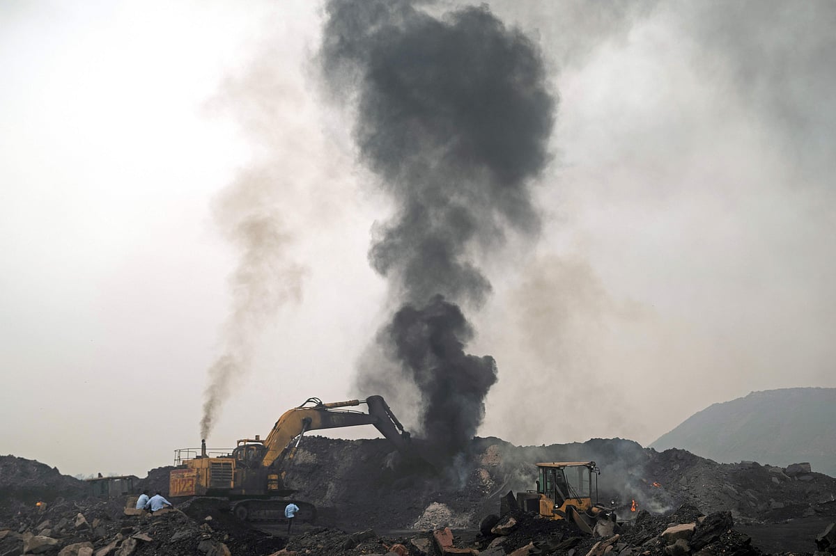 A plume of smoke rises as a worker operates a bulldozer to convey heaps of raw coal, excavated from an open-cast mine on the outskirts of Dhanbad, in India's Jharkhand state on 13 August, 2025