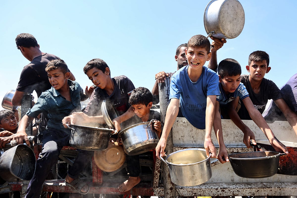 Palestinian boys extend their empty pots to receive cooked rice from charity kitchen in Gaza City on August 23, 2025