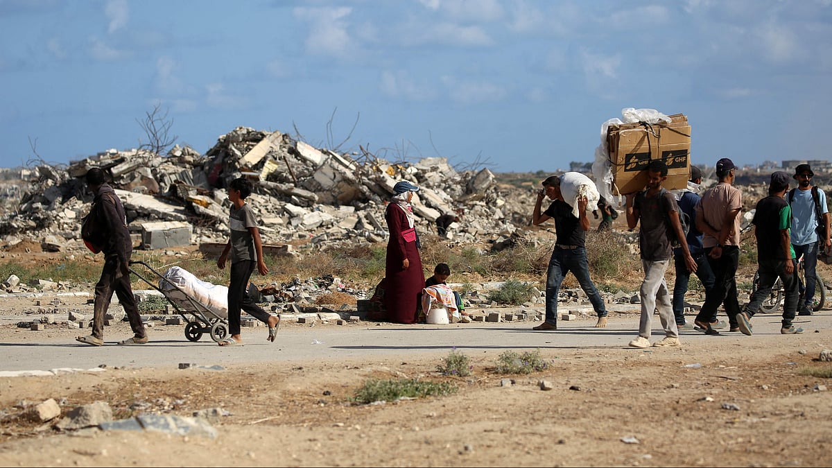 Palestinians carrying bags and empty cardboard boxes walk past a destroyed building as they return from a food distribution point run by the US and Israeli-backed Gaza Humanitarian Foundation (GHF) group, near the Netsarim corridor in the central Gaza Strip on 5 October, 2025