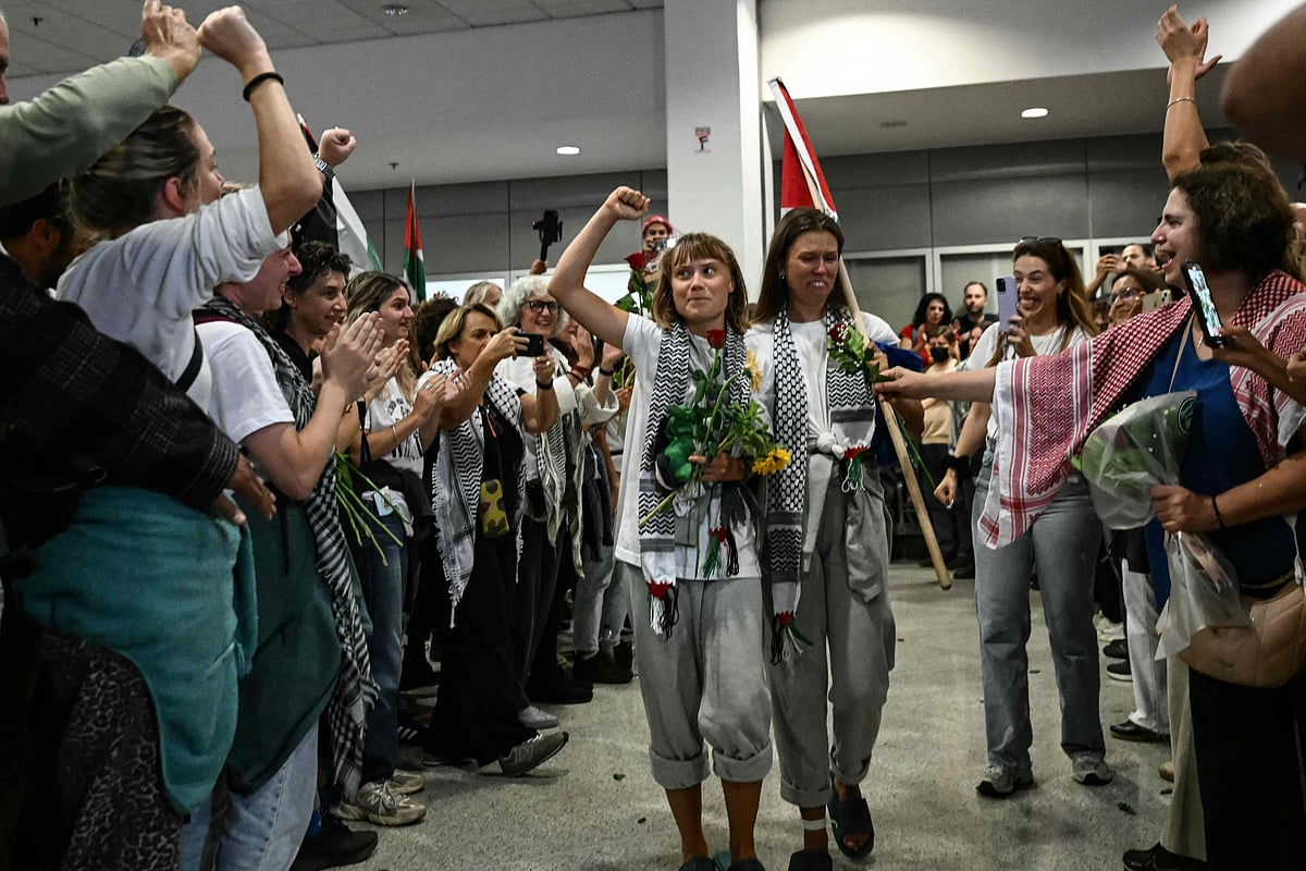Swedish climate campaigner Greta Thunberg raises her fist, upon arrival alongside activists who were sailing aboard vessels from the Gaza-bound aid flotilla before being stopped and detained by Israeli forces, greeted by a crowd of supporters, at the arrivals area of Athens International Airport on 6 October 2025.