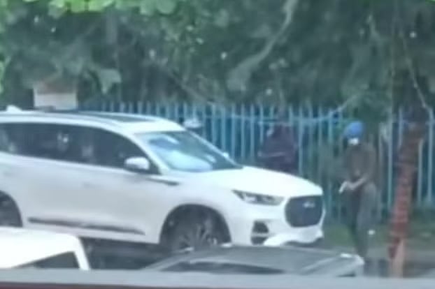 A man wearing a helmet shot arbitrarily at a sedan parked on the road