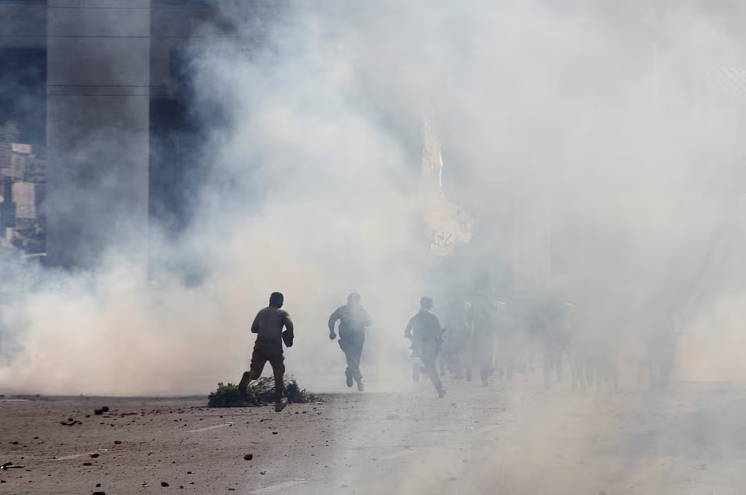 Police officers and supporters of Tehreek-e-Labbaik Pakistan (TLP) run amid tear gas fired by police during a solidarity march for Gaza in Lahore, Pakistan, 10 October, 2025.