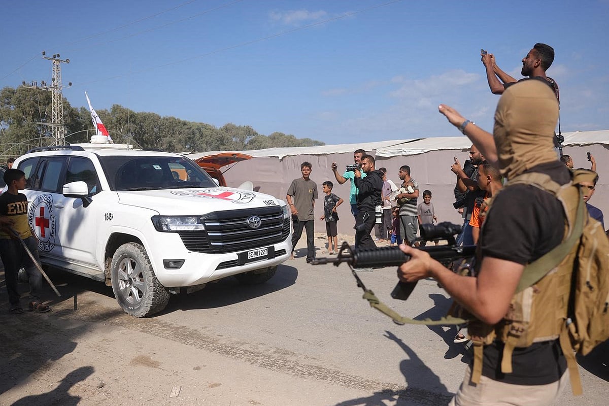 Hamas militants and civilians gather on the road as an International Red Cross vehicle arrive to transport the second batch of released Israeli hostages, south of Deir al-Balah in the central Gaza Strip on 13 October 2025.