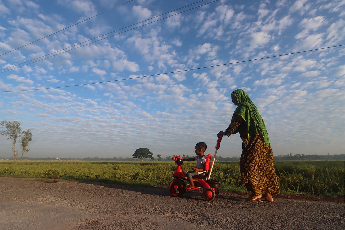 In the soft autumn morning, clouds gathered in the sky like tufts of cotton. On such a charming and serene morning, a grandmother is seen strolling along the road with her granddaughter and her toys. Bahadur Singh, Rangpur, 5 November.