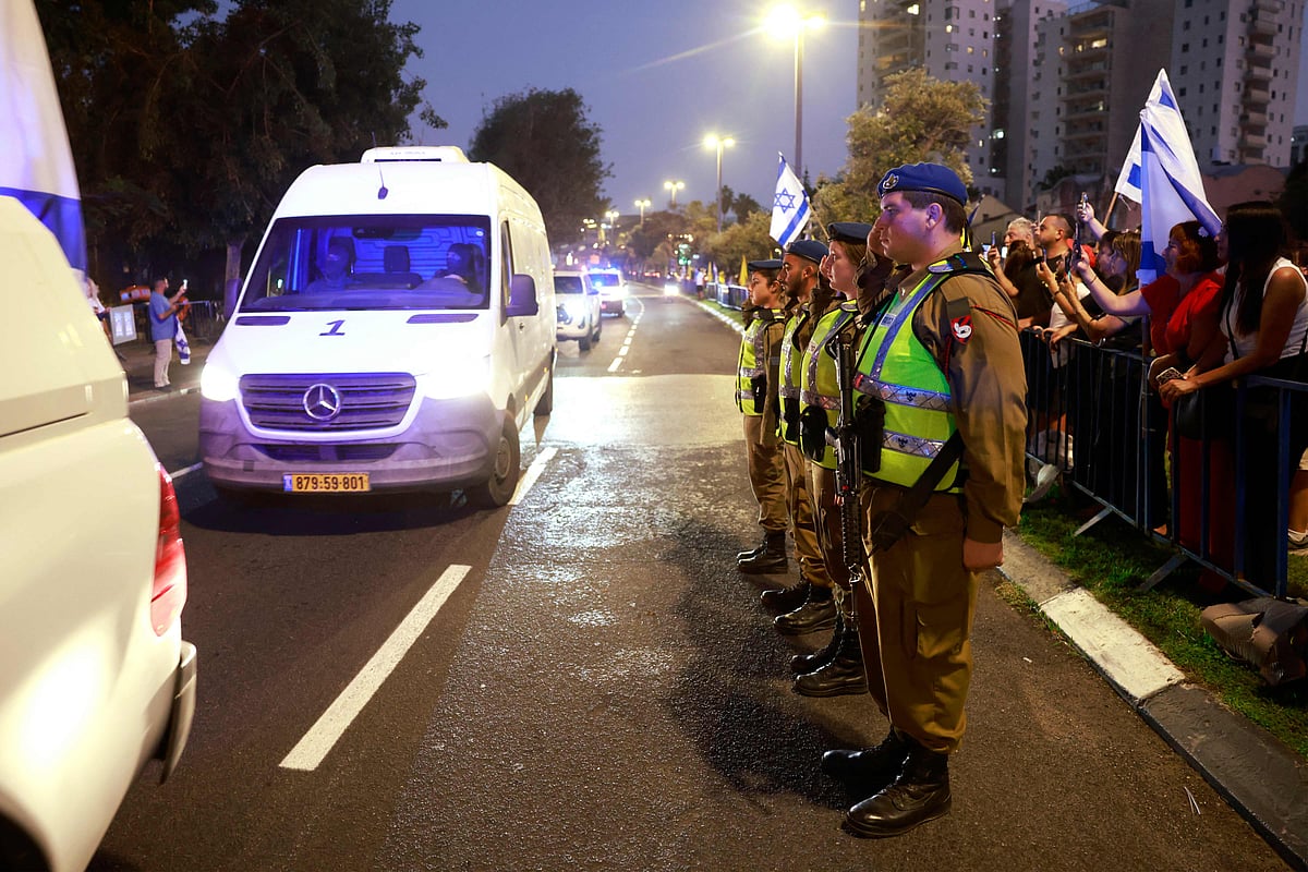 Israeli soldiers salute and people hold national flags as a van carrying human remains, thought to be those of Lt. Hadar Goldin, whom Hamas claims to have returned as part of a ceasefire agreement between Israel and Palestinian factions in Gaza, arrives at the National Center for Forensic Medicine in Tel Aviv on 9 November, 2025.