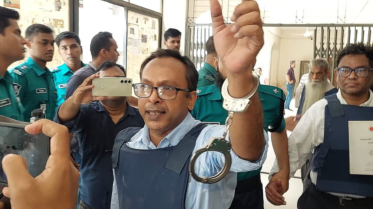 Journalist Monjurul Alam Panna raises his hand to show his handcuffs while being taken from the court.