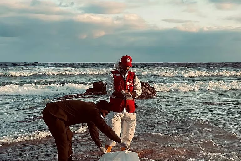 A member of the Red Crescent stands next to a body bag in a location given as near Surman, Libya, after a migrant boat capsized west of Libya's capital Tripoli, in this handout image released on 28 October, 2025.