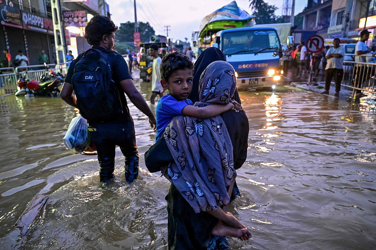 A woman carrying a child wades through a flooded street after heavy rainfall in Wellampitiya on the outskirts of Colombo on 30 November 2025