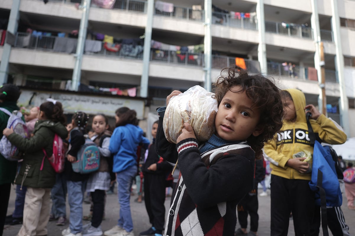 A Palestinian girl carries a bag of bread as others, many of whom are part of displaced families, gather in the yard of the UNRWA Deir al-Balah Joint School, west of Deir al-Balah, in the central Gaza Strip on December 6, 2025, under the first phase of the fragile US-brokered ceasefire between Israel and Hamas in the Gaza Strip