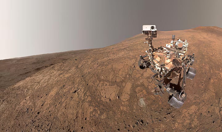 NASA's Perseverance rover took this selfie inside Jezero Crater in its northern hemisphere of Mars on 10 May, 2025. The small puff of dust left of center and below the horizon line is a dust devil, about 3 miles (5 kilometers) away.