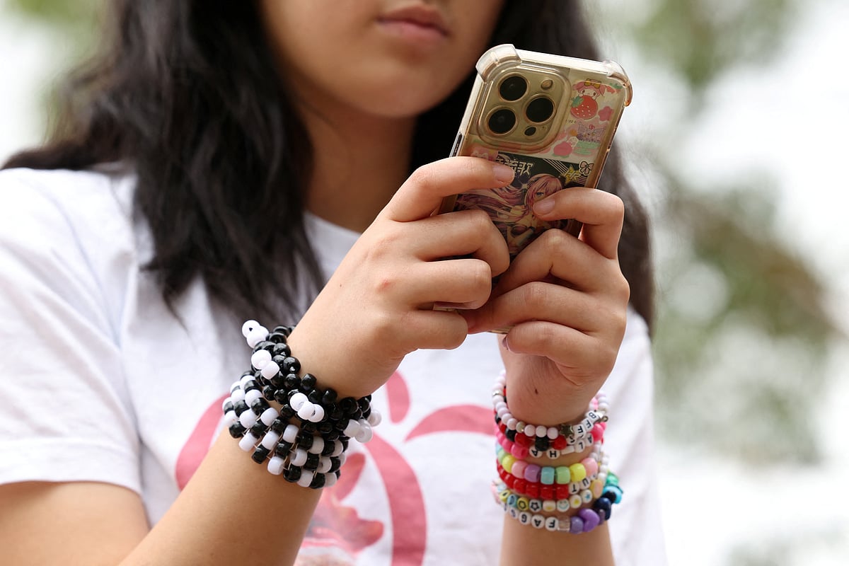 A teenager poses holding a mobile phone as law banning social media for users under 16 in Australia takes effect, in Sydney, Australia, 10 December 2025.