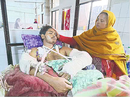 Abu Sufian lies on a hospital bed as his mother, Sufia Begum, sits by his side at the National Institute of Traumatology and Orthopaedic Rehabilitation (NITOR), known as Pangu Hospital, in Dhaka, on 28 December 2025.