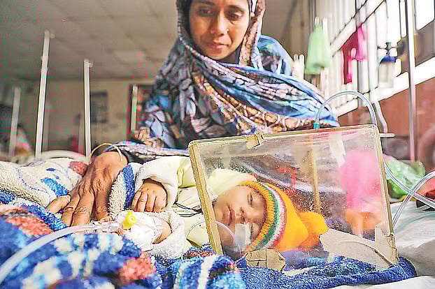 The grandmother sits beside the bed of two-and-a-half-month-old Farhana Islam, who is suffering from fever and breathing difficulties. The number of patients affected by cold-related illnesses is increasing at various hospitals in the capital. The photo was taken on Sunday morning at the Matuail Mother and Child Health Institute.