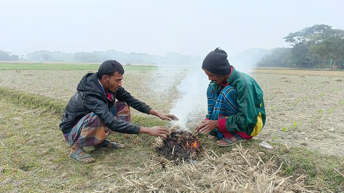 Farmers Sohel Mia and Humayun Kabir light a fire with straw to keep warm after being unable to work due to the cold, in Nikli upazila of Kishoreganj on 29 December 2025.