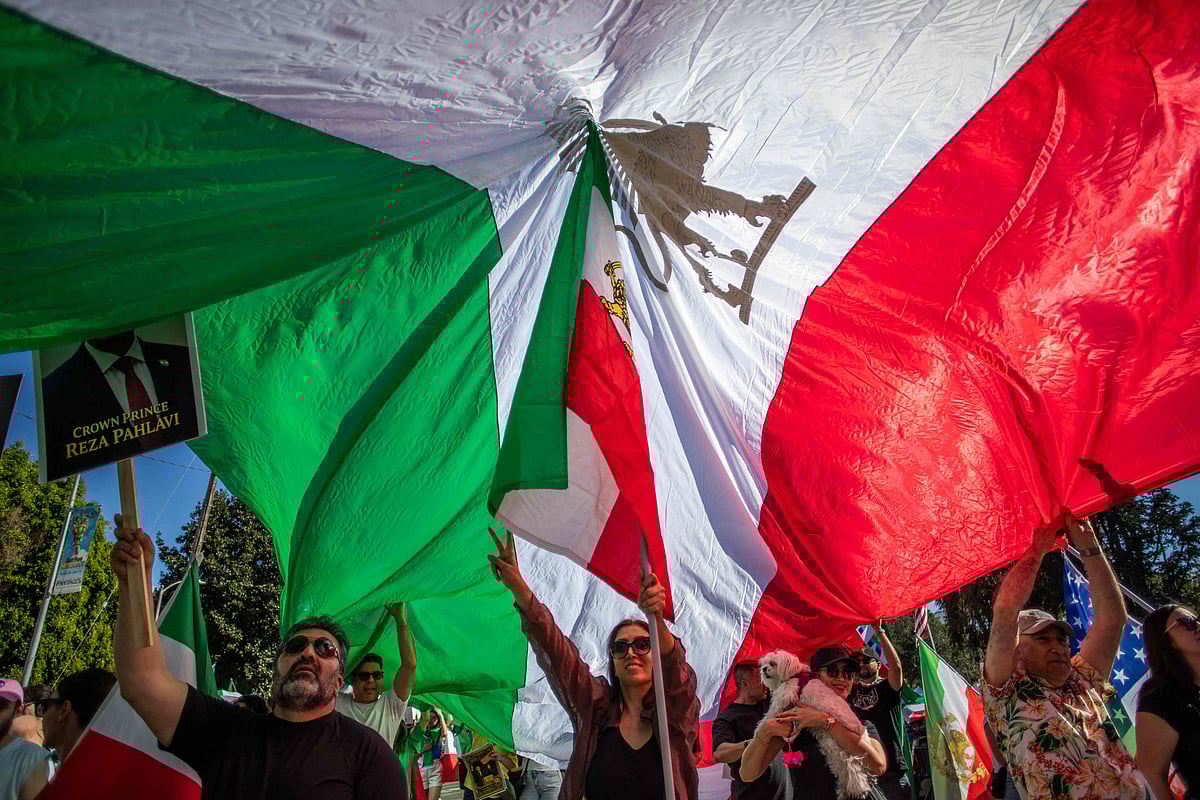 A woman walks under a Iranian pre-1979 Islamic Revolution flag as people wave flags while members of the Iranian community celebrate in front of the Federal Building in Los Angeles, on February 28, 2026. The US and Israel launched an attack of unprecedented scale against Iran on Saturday, reportedly killing more than 200 people, with Tehran launching a retaliatory missile barrage that sent people running for cover across the Middle East.