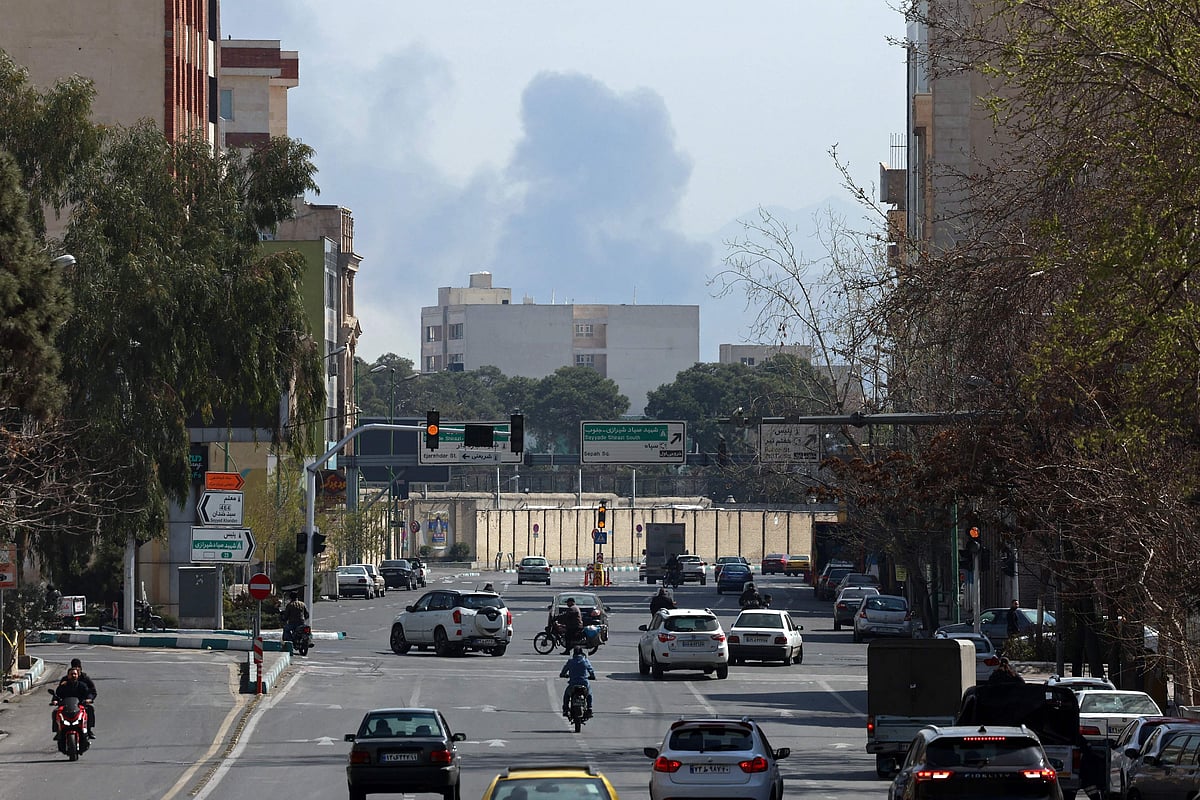 Commuters make their way along a busy street against the backdrop of a cloud of smoke rising after airstrikes in central Tehran on March 4, 2026