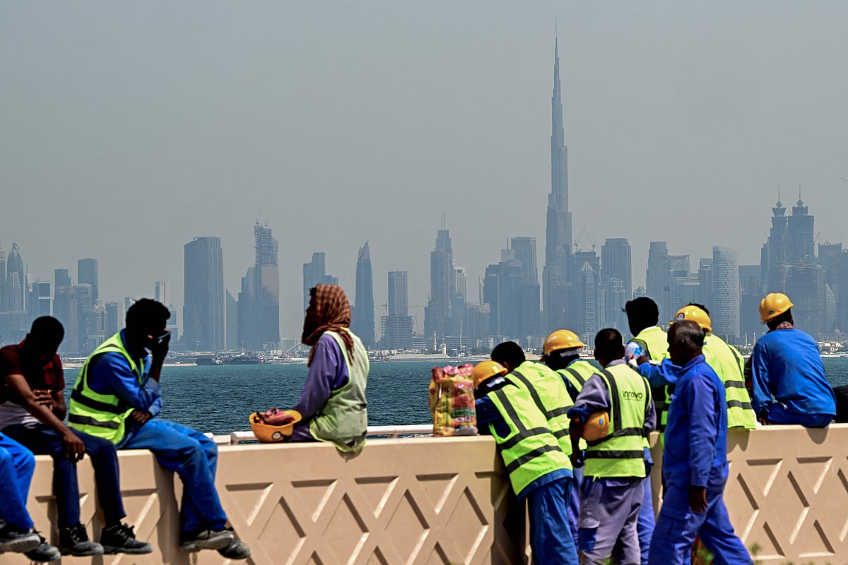 Workers sit on a wall against the backdrop of the city skyline as they take a break in Dubai on 11 March, 2026.