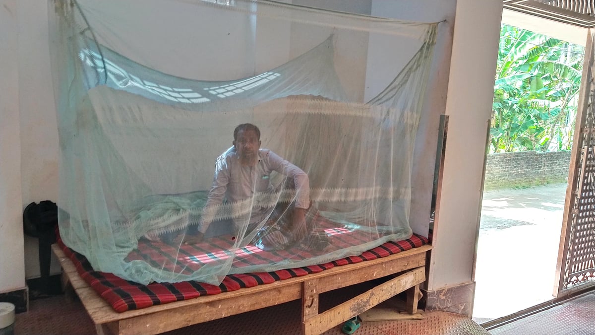Night guard Tajul Islam sitting under a mosquito net even during the daytime being tired of mosquitoes. On 8 April, 2026 at Satgara Mistripara area of Rangpur.
