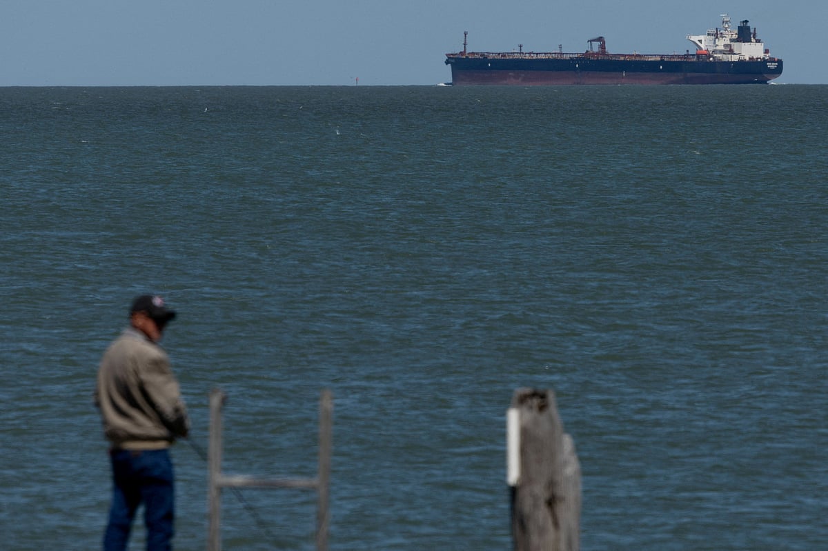 A man fishes as the Soho Square, a crude oil tanker sailing under the flag of Liberia, is at anchor in Galveston Bay as it makes its way to the Port of Houston, in Texas City, Texas, US on 18 March 2026.