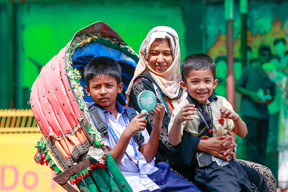 A child tries to get relief from the heat using the air from a handheld fan during a rickshaw ride as he returns home after classes in the heat in the University of Dhaka area on 20 April 2026.