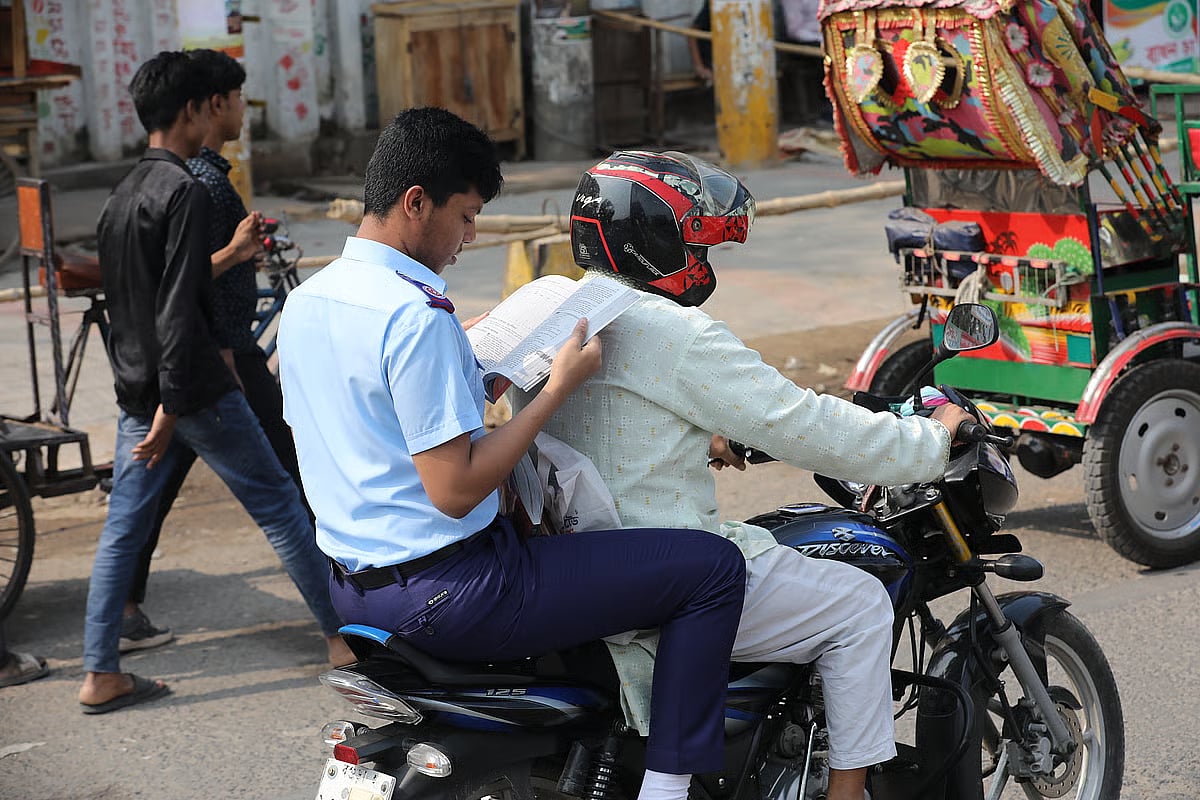 An SSC candidate glances through the pages of a book at the last moment while riding a motorcycle with a guardian.