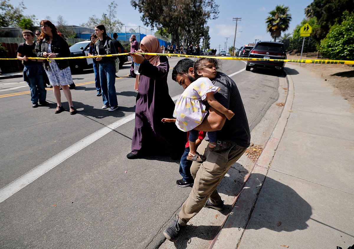 A parent passes under yellow tape cordoning an area, as he carries his child while they leave the mosque, at the scene of a shooting at the Islamic Center in San Diego, California, US, on 18 May 2026