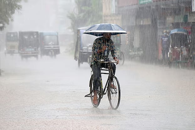 Heavy rain pours down. Amid the downpour, a man rides his bicycle with an umbrella over his head on his way to his destination.