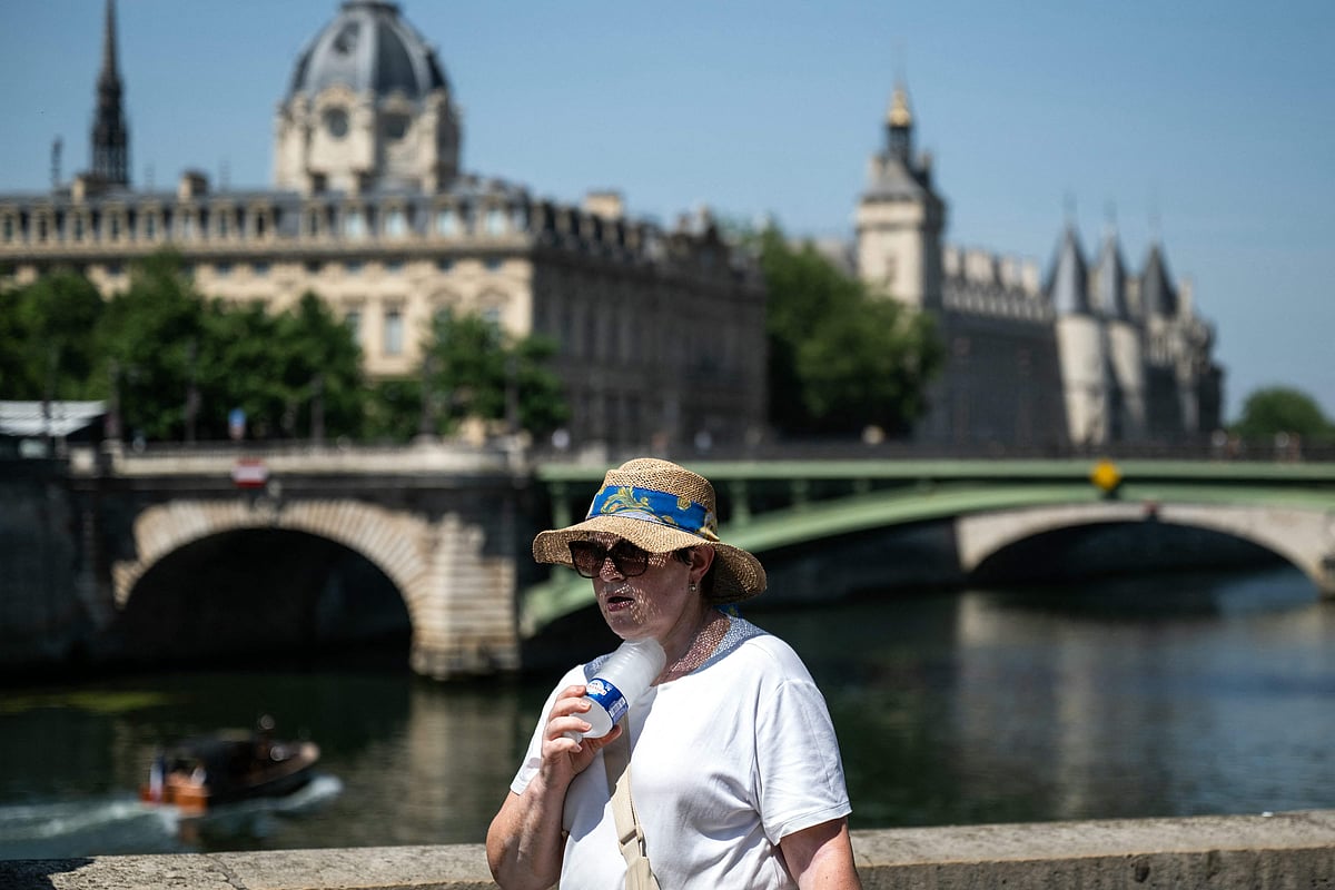 A woman with a hat cools off with a cold bottle of water on the Seine riverside with the Paris commercial court (L) and the Conciergerie buildings and the Pont Notre Dame in the background as France experiences a heat wave in Paris, France, on 21 June, 2026.