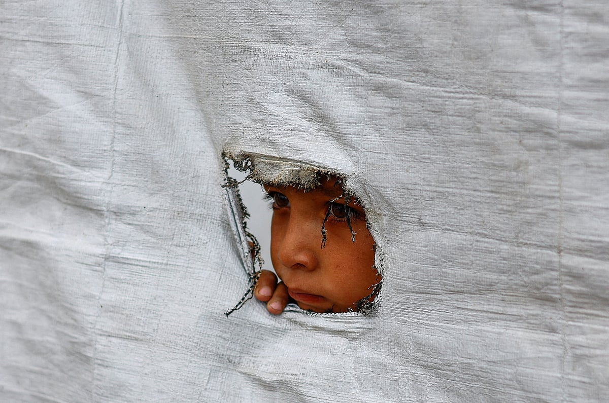 A displaced Palestinian boy peers through a tear in a tent wall, in Gaza City, 6 May 2026