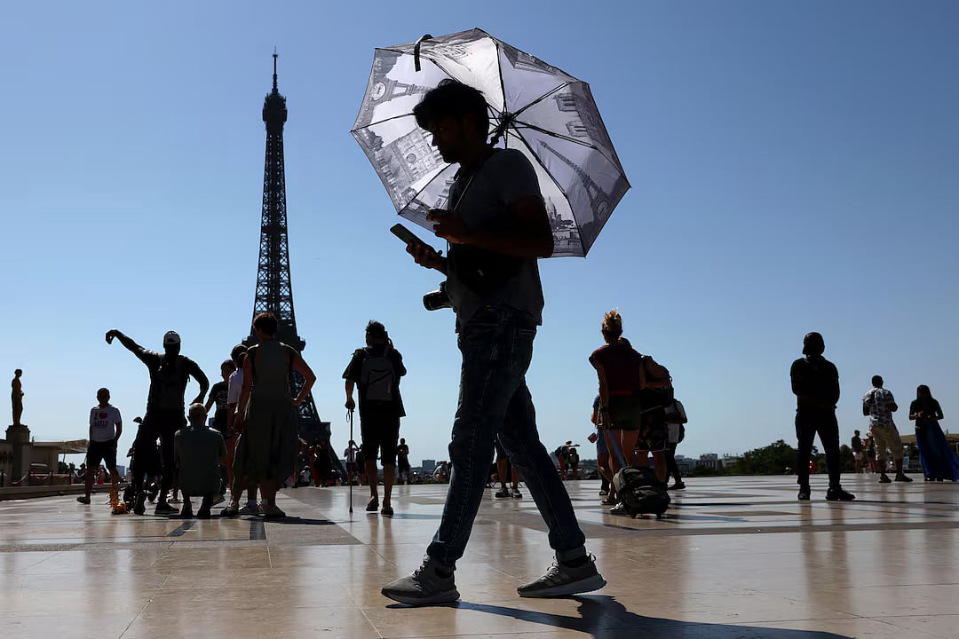 A tourist holding an umbrella to protect himself from the sun walks at Trocadero square next to the Eiffel Tower as an early summer heatwave hits Paris, France.