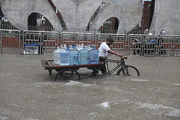 A van driver carries containers of safe drinking water through a waterlogged road amid heavy rain in Kakrail, Dhaka, on Sunday.