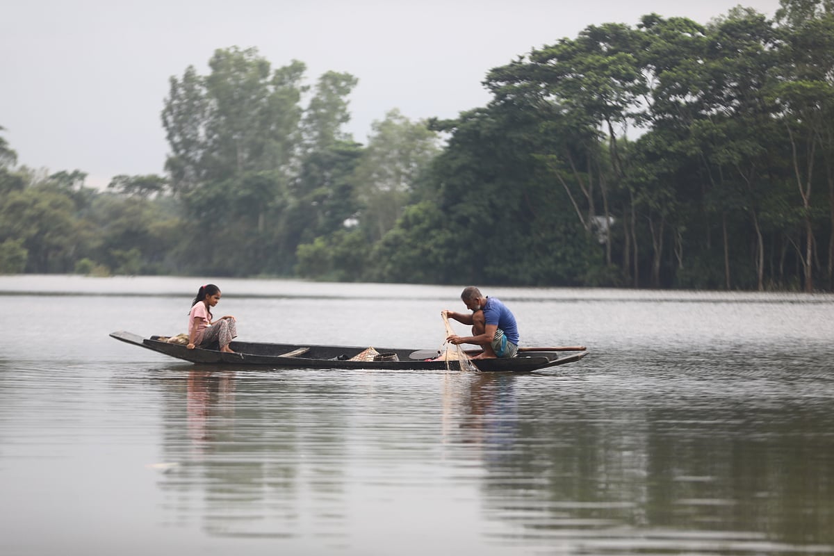 A father catches fish with a net set from his boat in the haor waters, while his daughter sits in front of watching. Ufhar Haor, Sylhet, 13 July.