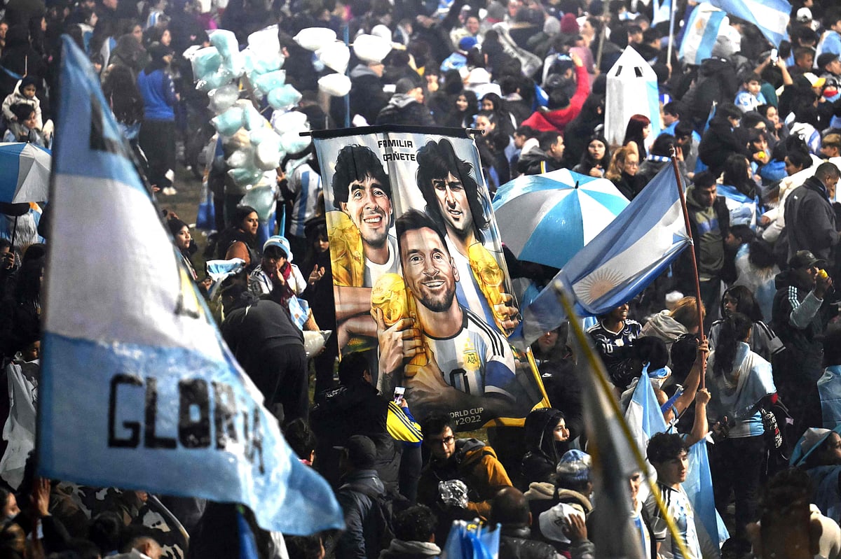Fans hold a banner depicting Argentine football legends Diego Maradona, Mario Kempes and Lionel Messi holding FIFA World Cup trophies as supporters gather near the Argentine Football Association (AFA) training camp in Ezeiza, Buenos Aires Province, on 20 July, 2026, while awaiting the arrival of Argentina's national football team from the United States following its defeat in the 2026 FIFA World Cup final.