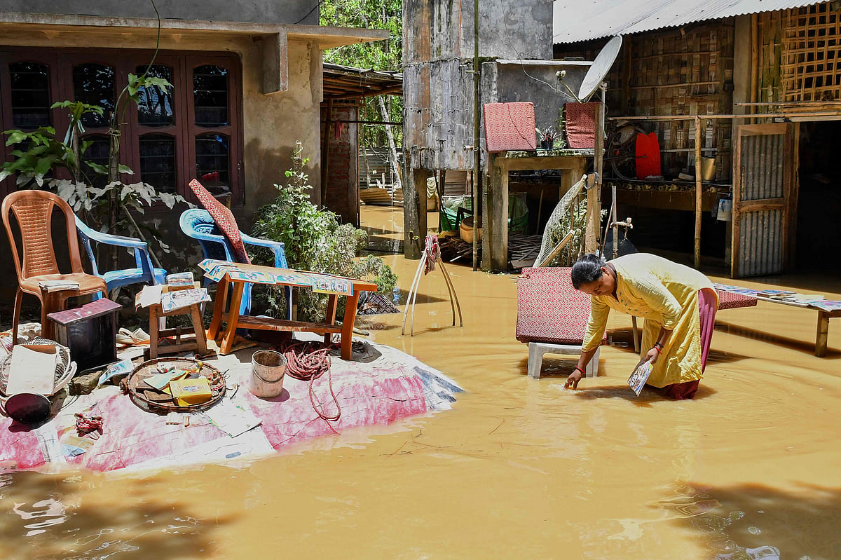 A woman salvages belongings outside her house damaged by floodwaters following heavy rains in Assam's Jorhat district on 21 July, 2026.