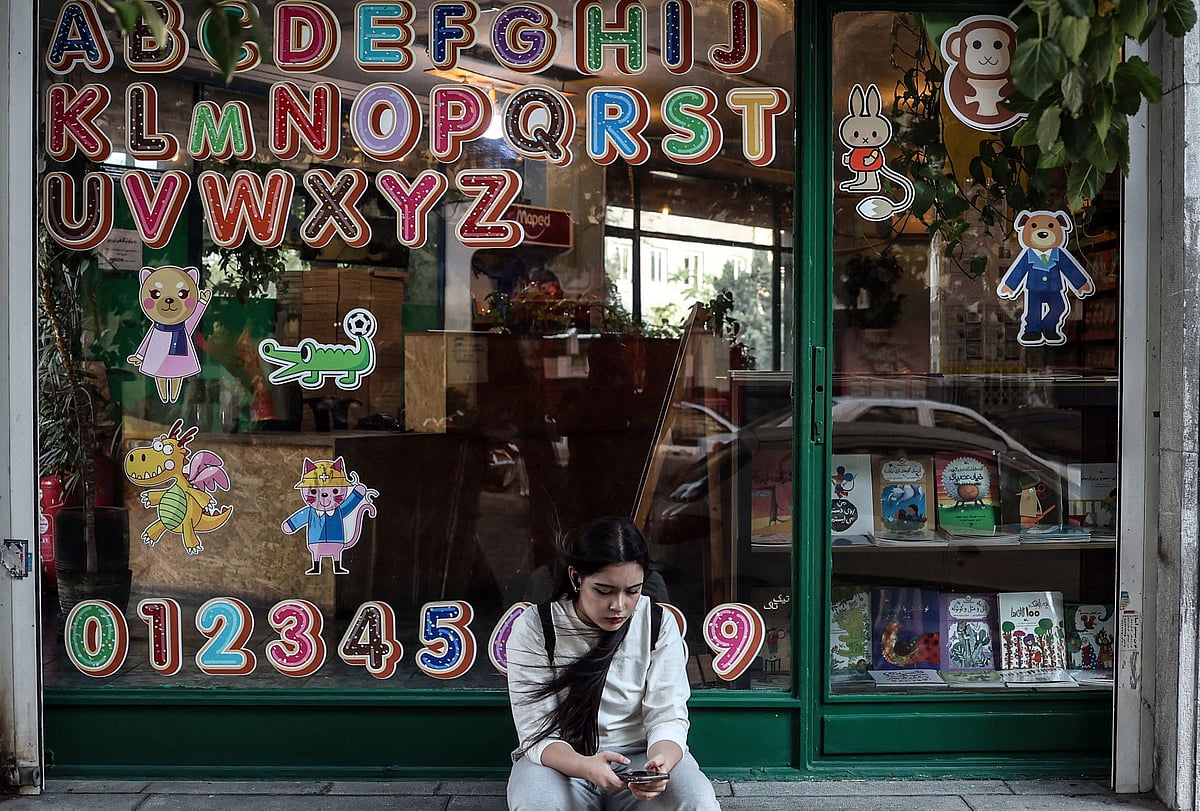 A girl sits looking at her mobile phone in front of an english bookshop in Tehran on 7 September, 2026. Testing has been suspended in Iran since 1 September following the latest US sanctions, announced last week as part of what Washington calls its "economic asphyxiation" of Iran amid the Middle East war that broke out on 28 February.