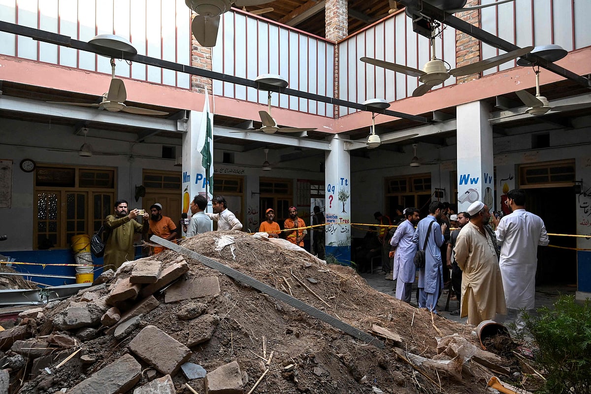 People gather around debris and rubble lying in the courtyard of a school following a roof collapse, in Peshawar on 15 October 2026. The roof of a school collapsed in Pakistan's northwestern city of Peshawar, killing a teacher and 32 students, mostly aged under 14, health officials said on October 15, as residents and rescuers scrambled to pull children from the rubble.
