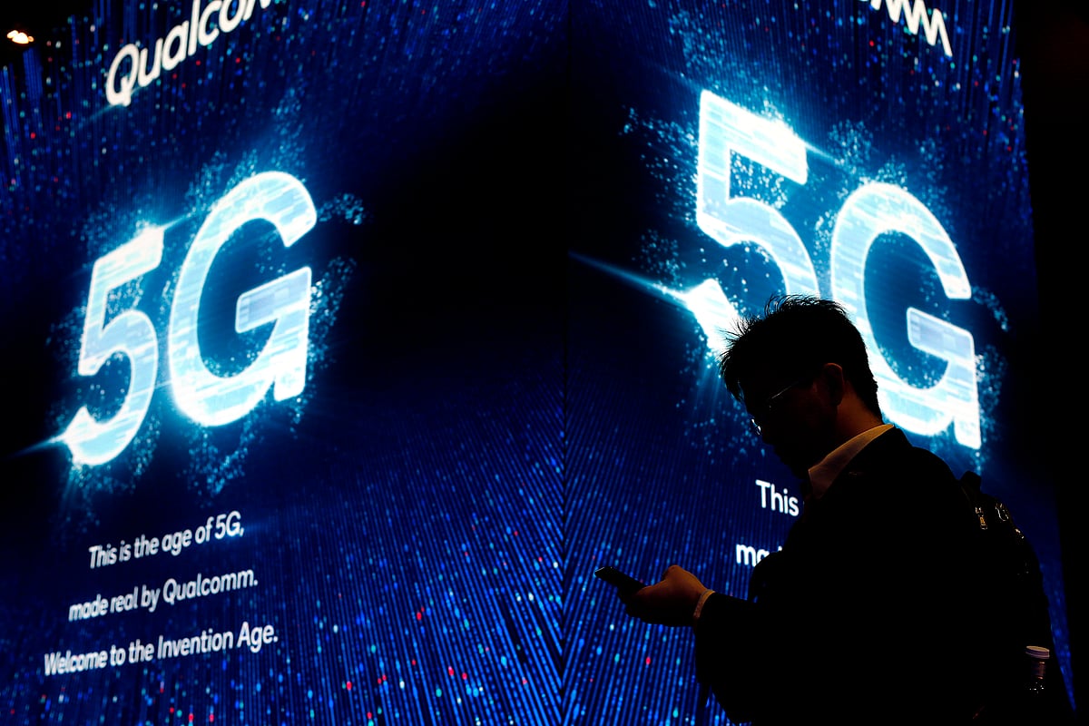 A man uses his phone next to a 5G sign at the Qualcomm stand at the Mobile World Congress (MWC) in Barcelona.