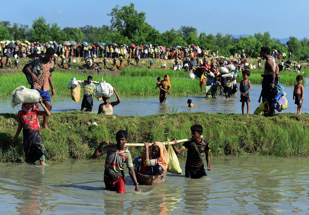 In this file photo taken on 16 October 2017 Rohingya refugees carry a woman over a shallow canal after crossing the Naf River as they flee violence in Myanmar to reach Bangladesh in Palongkhali near Ukhia
