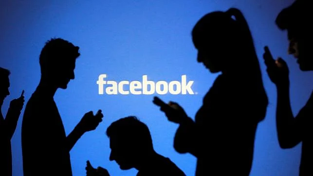 People are silhouetted as they pose with mobile devices in front of a screen projected with a Facebook logo, in this picture illustration on 29 October 2014. 